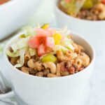 Up close picture of a bowl of cheeseburger casserole topped with lettuce pickle and tomato