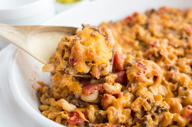 Up close picture of cheeseburger casserole in white baking dish with spoon holding a portion