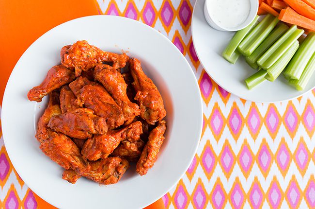 Overhead picture of buffalo chicken wings in a large white bowl sitting on a colorful tablecloth