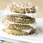 An up close picture of baked fried green tomatoes stacked on a white platter and drizzled with sauce