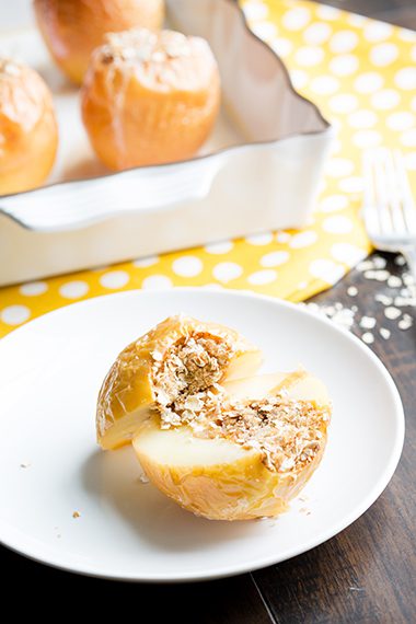Baked apples sliced in half on a white sauceer with oatmeal inside