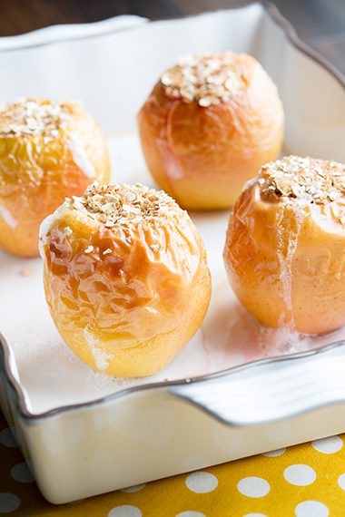 Four baked apples in baking dish on white yellow napkin
