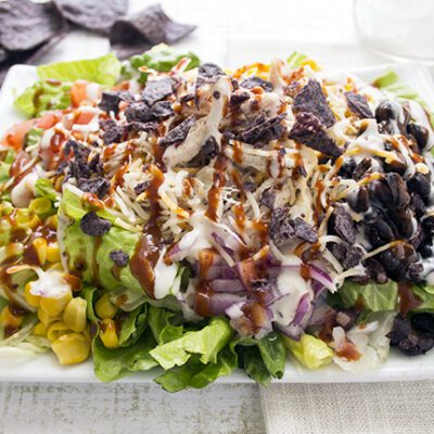 An up close picture of a plate of barbecue chicken salad topped with onions black beans corn and shredded chicken