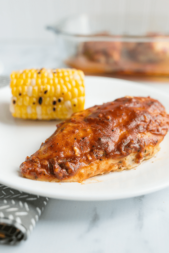 Baked chicken with bbq ranch seasoning on a white plate with grilled corn