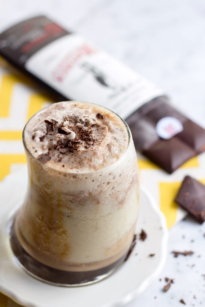 Banana protein shake with chocolate in a tall glass with chocolate bar in background