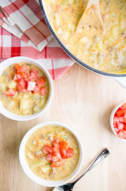 2 bowls of soup sitting on wooden surface with stockpot full of cheeseburger soup in background