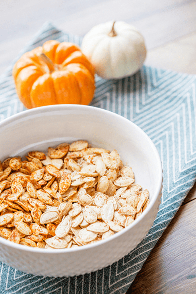 Large white bowl filled with two flavors of roasted pumpkin seeds sitting on a blue napkin
