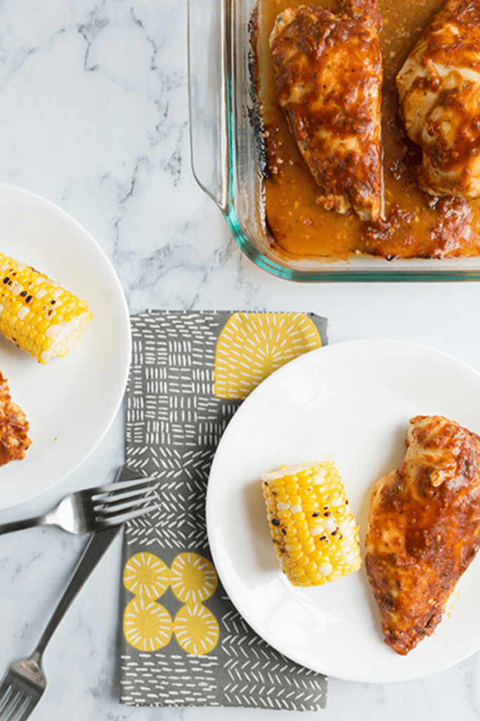 Overhead picture of a bbq ranch baked chicken breasts on a white plate with corn on the side
