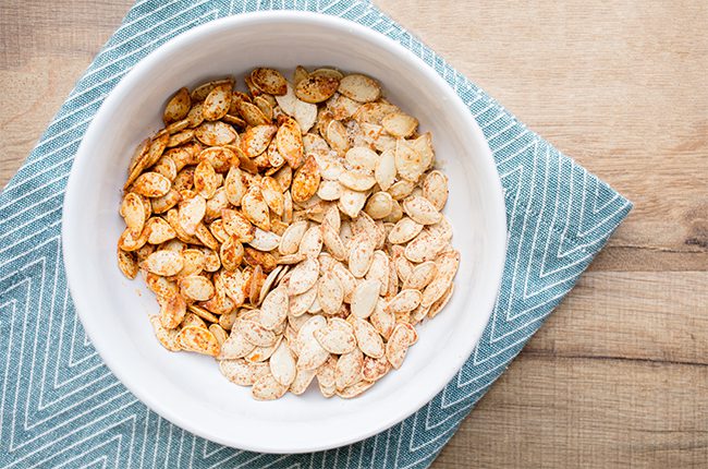Overhead picture of pumpkin seeds in a white bowl on a blue napkin
