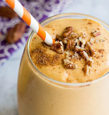 Single glass of pumpkin smoothie topped with chopped pecans, cinnamon and an orange and white paper straw