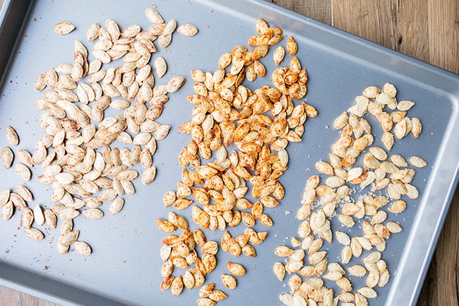 Pumpkin seeds seasoned and laying on a baking sheet