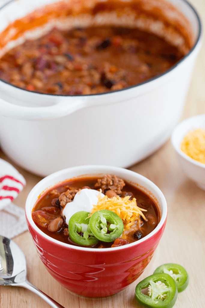 Red bowl filled with turkey chili sitting in front of large white stockpot of chili