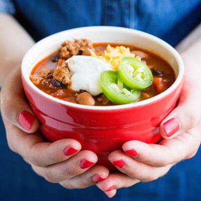 Red bowl of turkey chili being held by a woman in blue