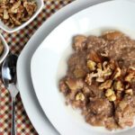 Square overhead image of apple pie oatmeal in white bowl topped by nuts