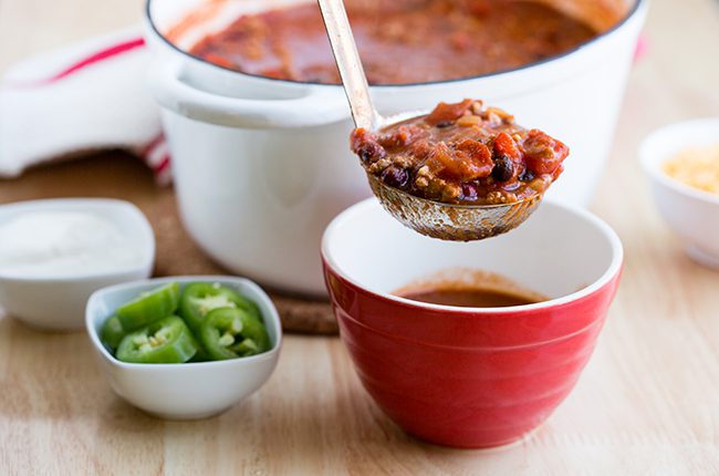 White stockpot full of turkey chili sitting behind a red bowl of chili
